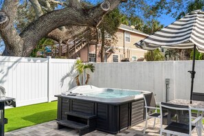 Ein Garten mit Whirlpool, Terrassentisch und einem gestreiften Sonnenschirm.