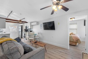 Ein modernes Wohnzimmer mit Sofa, Couchtisch und Essbereich mit Stühlen. Ein Deckenventilator, ein flachbildfernseher an der Wand und eine durchgehende Küche sind ebenfalls zu sehen.