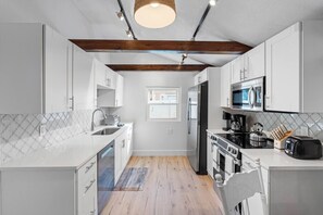 Een moderne keuken met witte kastjes, een houten plafond, een inbouwoven en een magnetron.