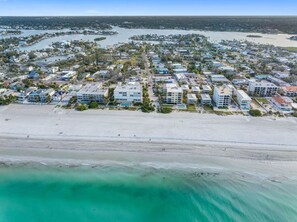 Luchtbeeld van een kustgebied met woonhuizen, panden aan het strand, een zandstrand en een jachthaven.