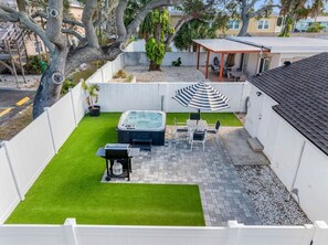 Een achtertuin met kunstgras, een hottub, tuinmeubels en een overdekt zitgedeelte.