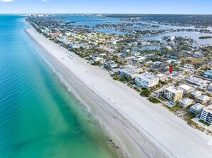 An aerial view of a coastal town with a long sandy beach, residential buildings, and a marina. - July Deals - Pet Friendly and Hot tub! Cottage (Indian Rocks Beach)