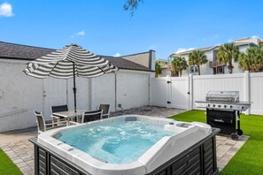 A backyard with a hot tub, a grill, a striped umbrella, and a patio table with chairs. - July Deals - Pet Friendly and Hot tub! Cottage (Indian Rocks Beach)