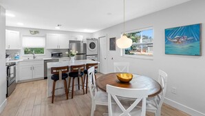 Une cuisine moderne avec des meubles blancs, des appareils en acier inoxydable et un coin repas comprenant une table et des chaises en bois.