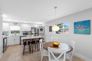 A modern kitchen with white cabinetry, stainless steel appliances, and a dining area with a wooden table and chairs. - July Deals - Pet Friendly & Hot Tub! Suite A (Indian Rocks Beach)