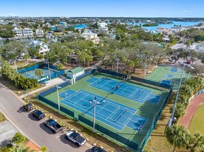 Un complex de pistes de tennis amb diverses pistes, una zona d'aparcament i edificis residencials al voltant.