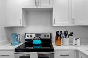 A kitchen with white cabinets, a black stove, a blue kettle, a coffee maker, a knife block, and a toaster. - Sept Deals! Pet Friendly & Hot Tub! Suite A (Indian Rocks Beach)