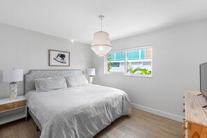 A bedroom with a bed, bedside lamps, a picture on the wall, a window with a view, and a ceiling light fixture. - July Deals - Pet Friendly and Hot tub! Suite B (Indian Rocks Beach)