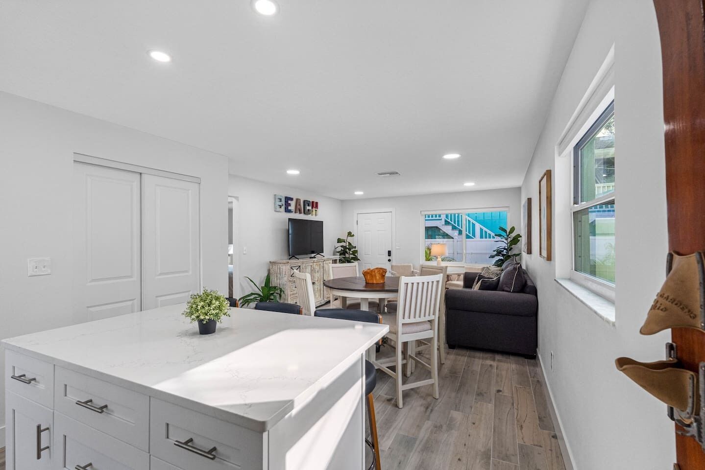 Une cuisine moderne avec des meubles blancs, un coin repas comprenant une table et des chaises, et une vue sur un escalier extérieur.