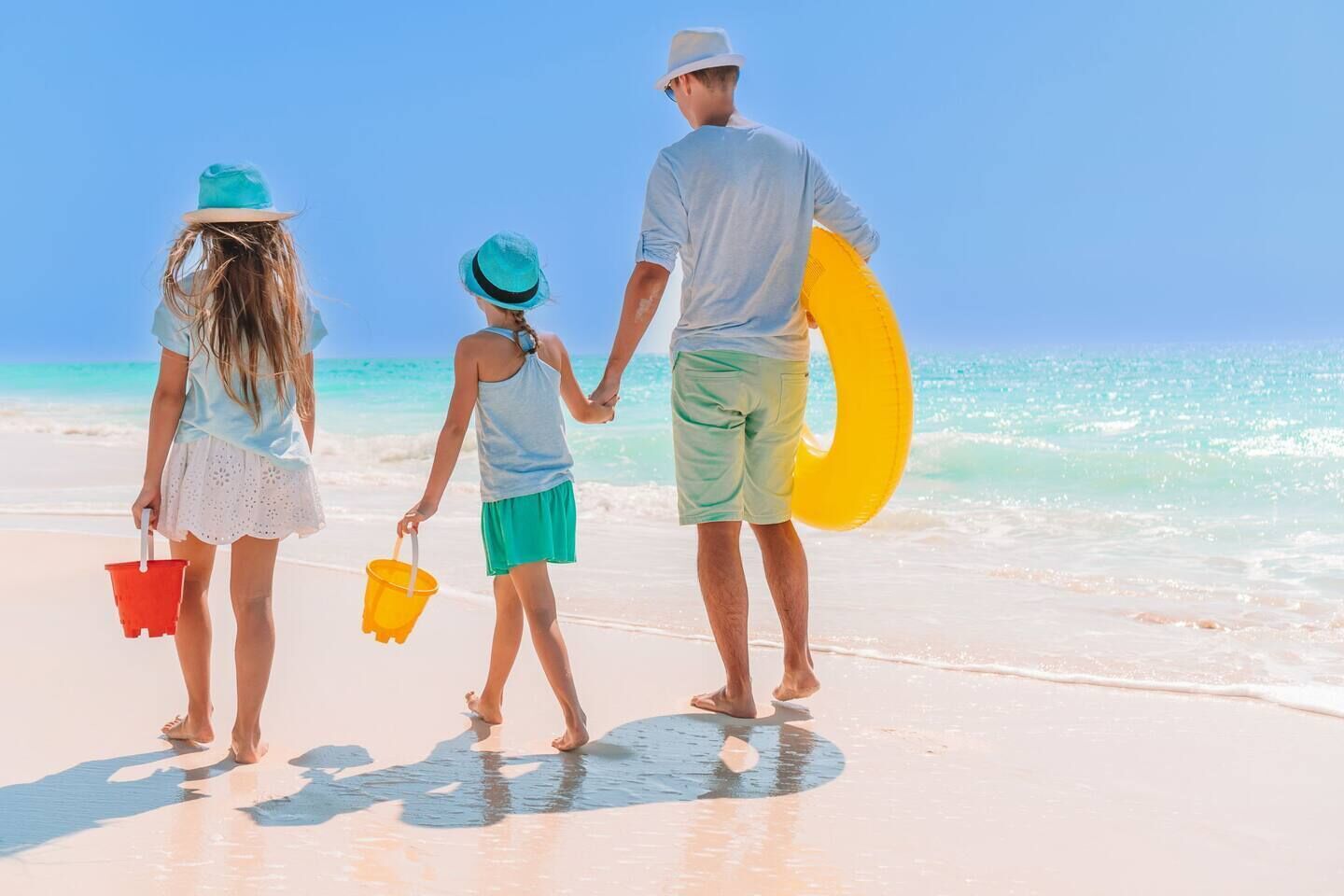 Una família passeja per la platja sota un cel clar.