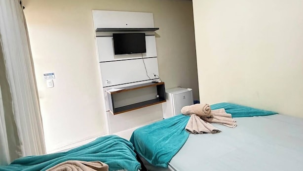 Habitación de hotel con dos camas, un televisor de pantalla plana montado en la pared, un escritorio pequeño con una silla y una ventana con cortinas.