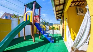 Un parque infantil con un tobogán y escaleras, rodeado por un edificio amarillo con una cortina blanca.