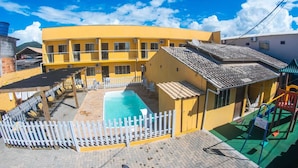 Un edificio amarillo con piscina, un patio amurallado y un parque infantil.