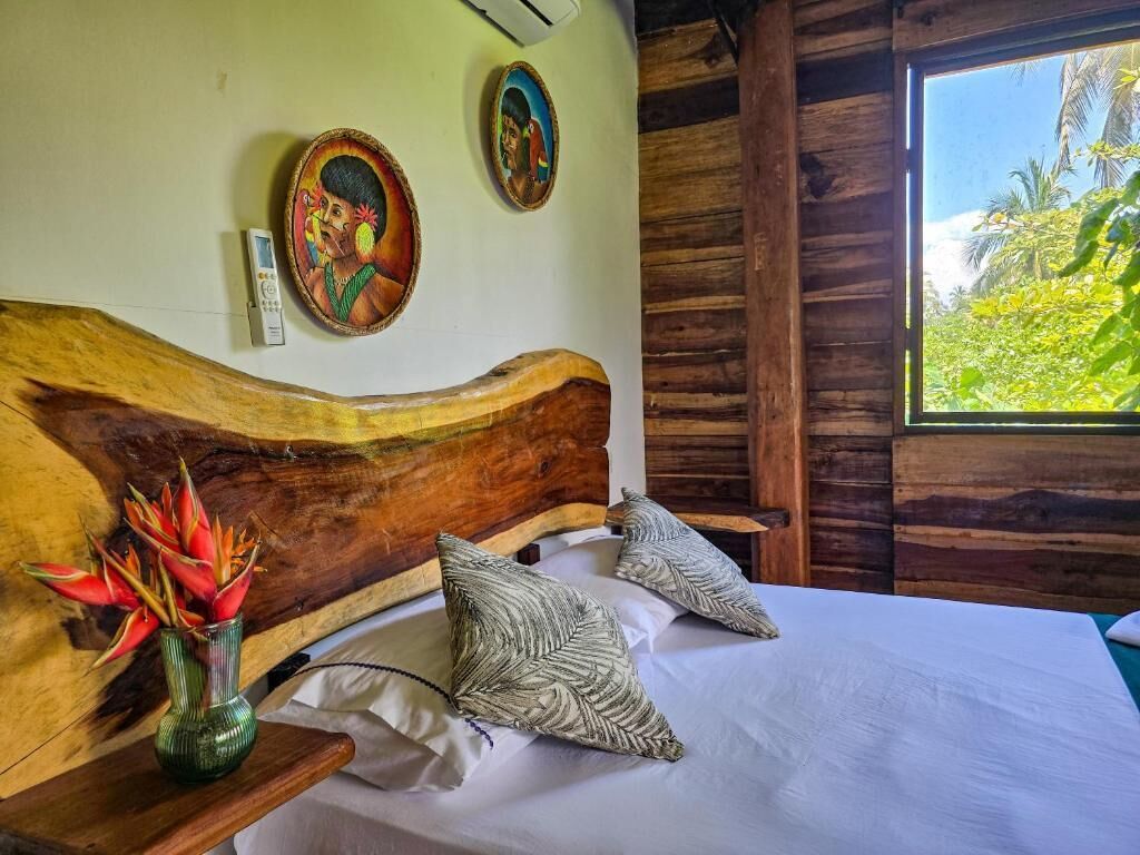 A wooden-framed room with a bed, pillows, a vase with flowers, and wall art.