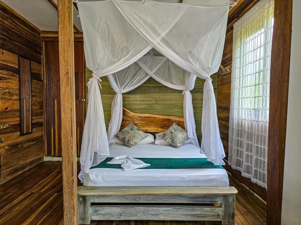 Una cama con dosel, paredes de madera y un ventanal con persianas.