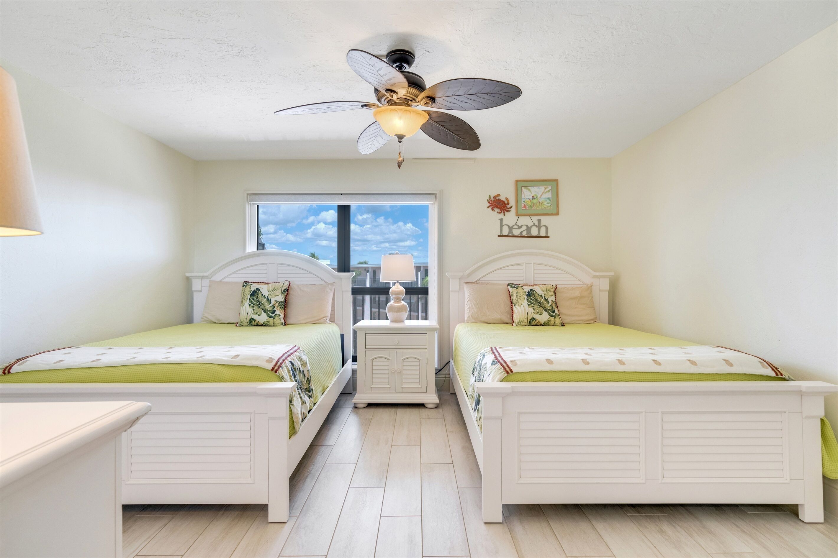A bedroom with two beds, a ceiling fan, a window, and a view of the sky.