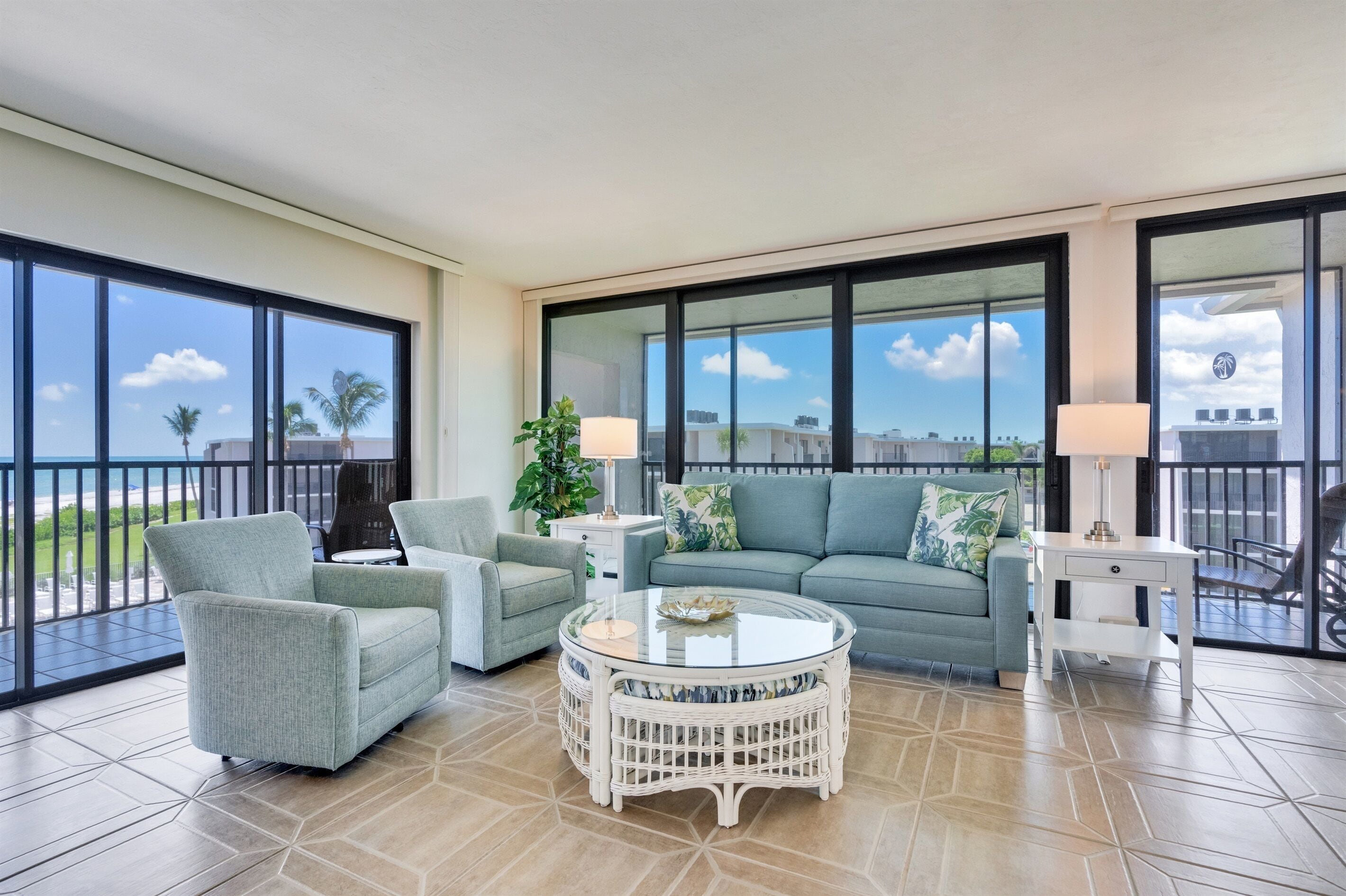 Un balcon spacieux offrant une vue sur les palmiers et les immeubles, aménagé avec un canapé, des fauteuils et une table ronde.