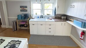 Een keuken met witte kastjes, een gasfornuis, een spoelbak en een raam met uitzicht op het omliggende landschap.