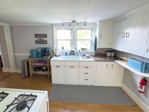 A kitchen with white cabinets, a gas stove, a sink, and a window with a view of the outdoors.