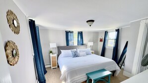 Een slaapkamer met een bed, nachtkastjes, een bankje en gordijnen.