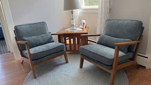 Een kamer met twee grijze fauteuils, een houten tafel, een lamp en een kamerbreed tapijt met dessin.