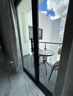 Ein moderner Balkon mit Glastür, rundem Tisch und einem Stuhl.