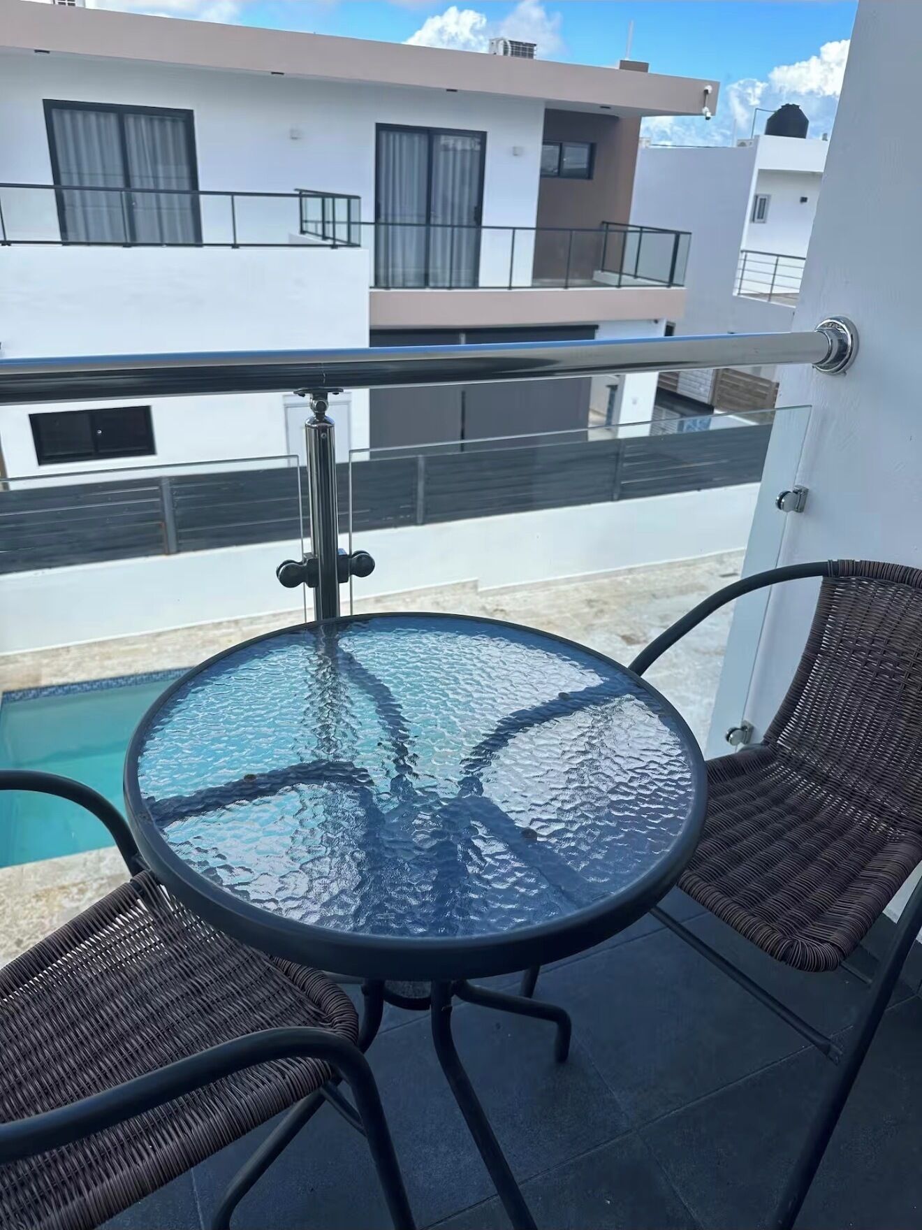 Ett bord med glasskiva och två flätade stolar på en balkong med utsikt över poolen.