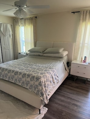 Ein Schlafzimmer mit einem Bett, einem Nachttisch, einem Deckenventilator und einem Fenster mit Vorhängen.