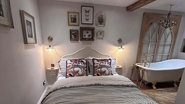 Ein Schlafzimmer mit einem großen Bett, einer Badewanne im Vintage-Stil und Wandleuchten.