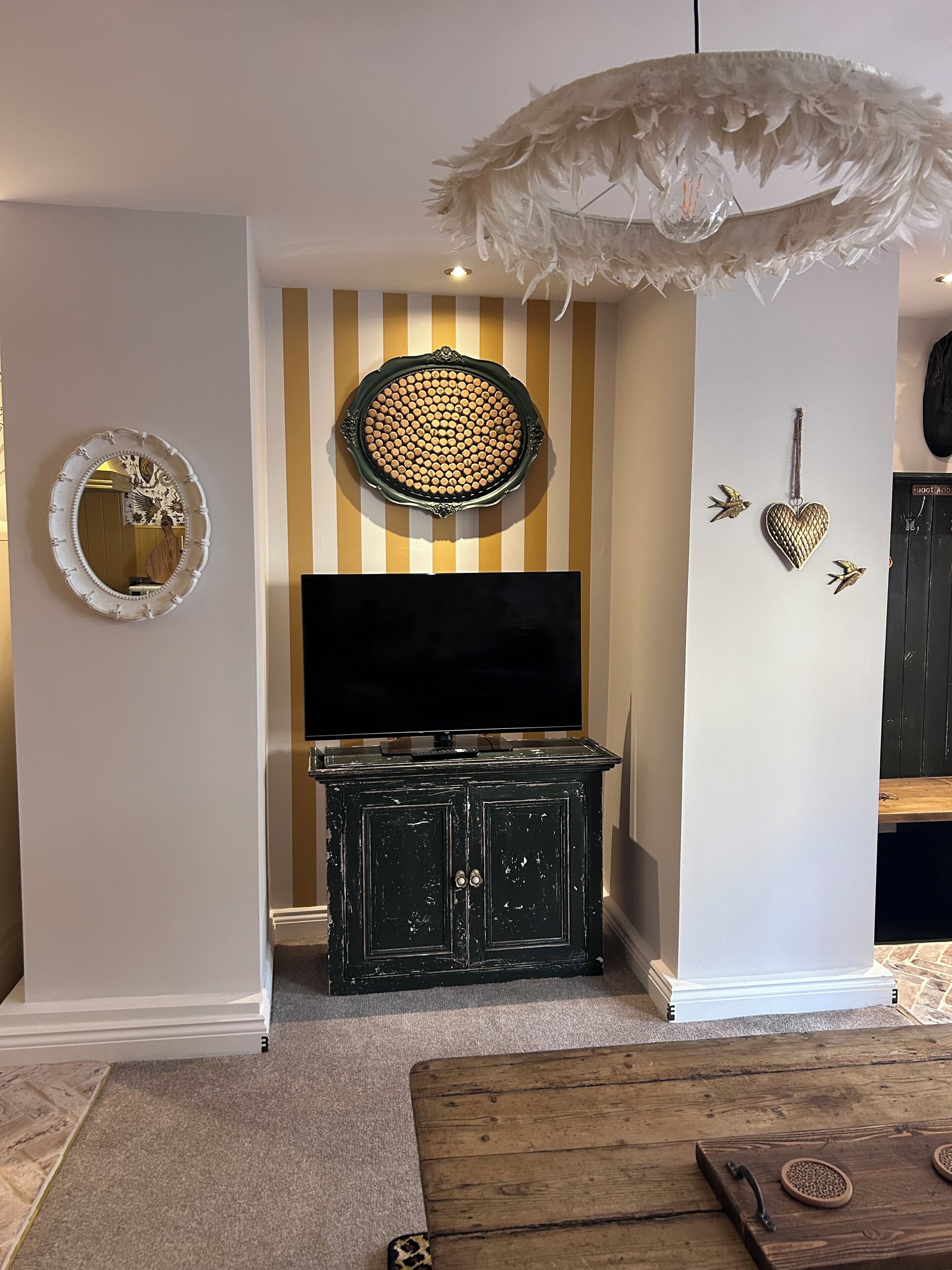 A room with a television, decorative wall art, a feathered light fixture, and a wooden cabinet.