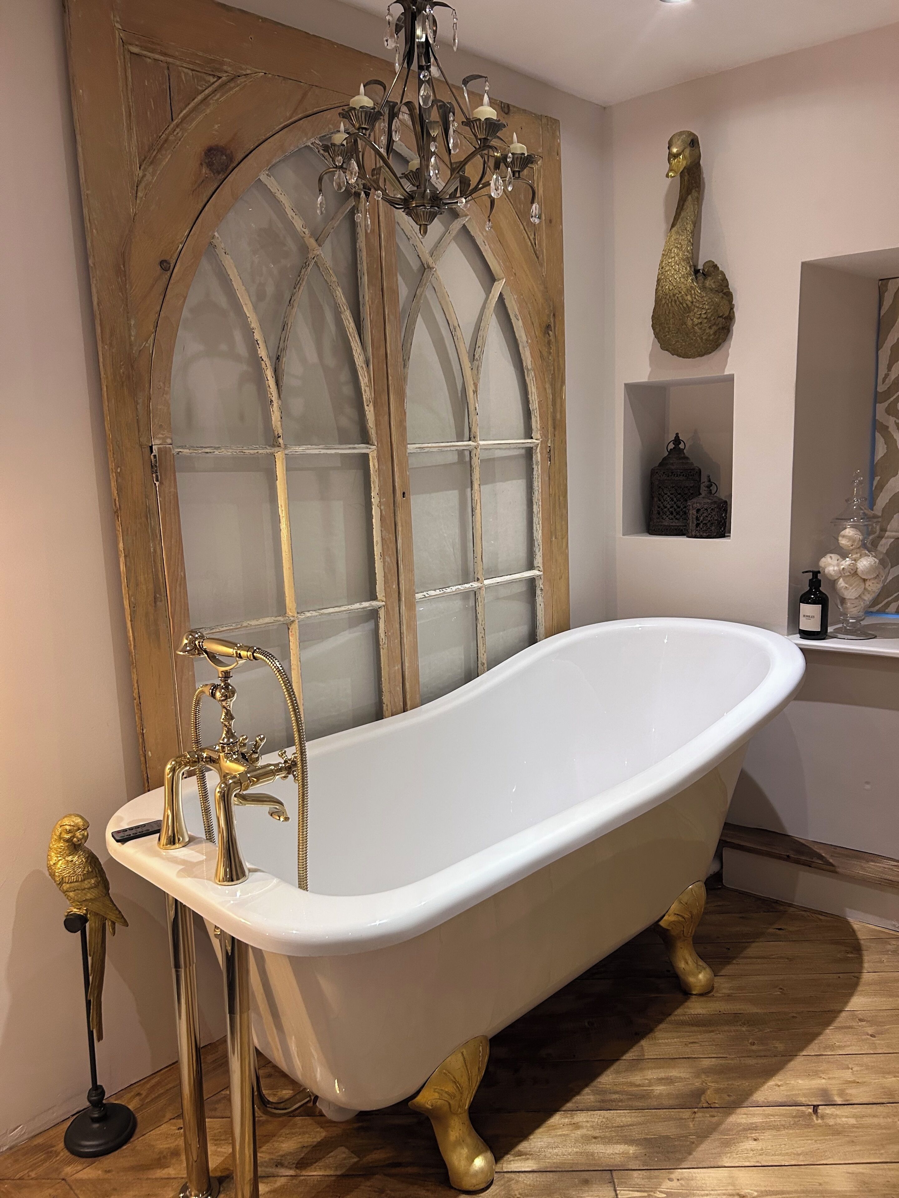 A bathroom with a freestanding bathtub, a chandelier, and a wooden-framed window.