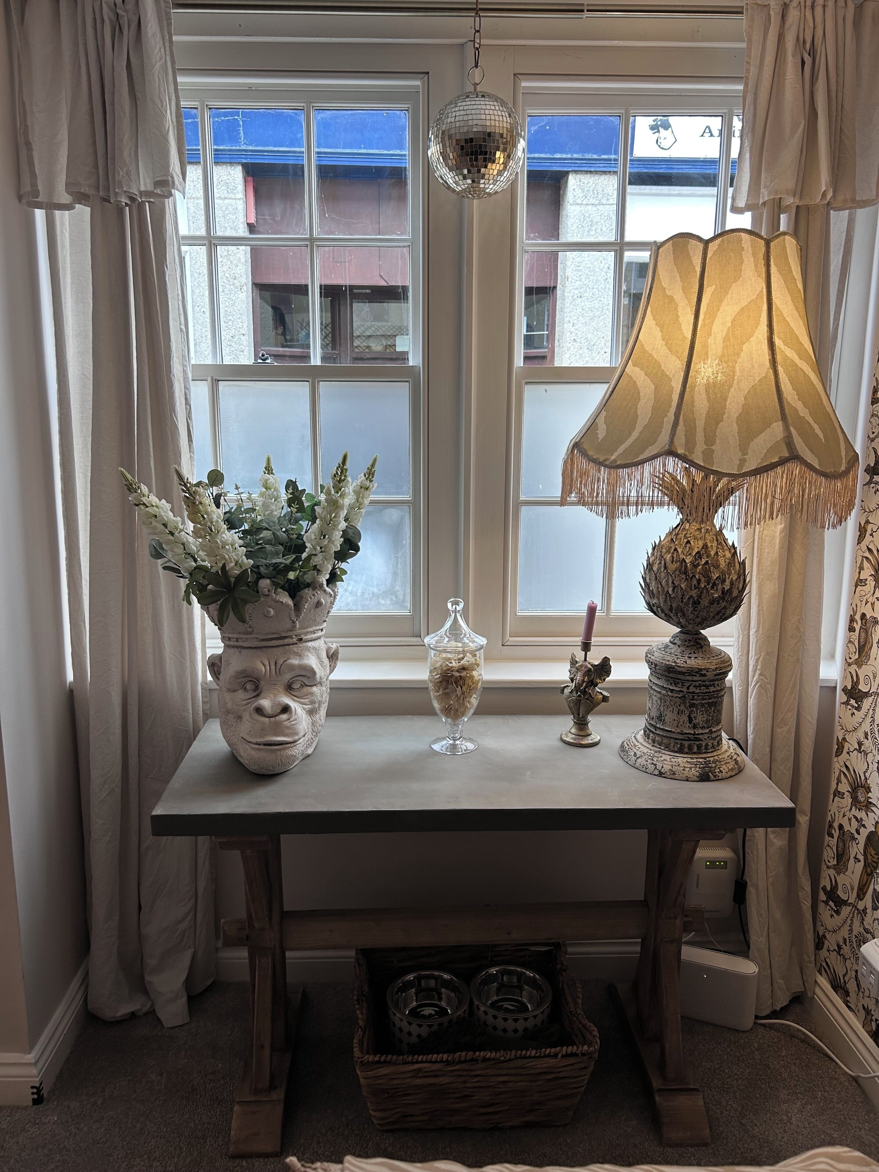A room with a table featuring a potted plant, a glass container, and a decorative lamp.