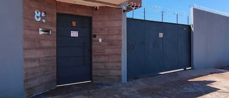 Un edificio con una puerta metálica cerrada, un ventanal pequeño y una valla de seguridad con alambre de púas.
