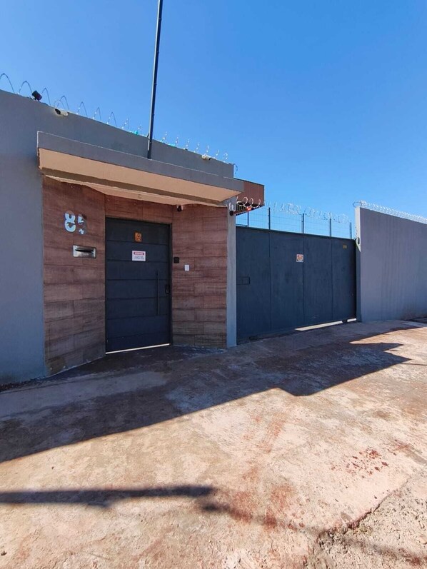 A building with a closed metal door, a small window, and a security fence topped with barbed wire.