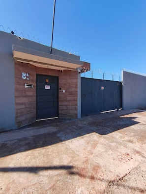 A building with a closed metal door, a small window, and a security fence topped with barbed wire.