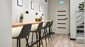 A reception area with a wooden counter, four grey chairs, framed pictures on the wall, a potted plant, and a door with a sign. - Nomad Boutique Hostel  (Tallinn)