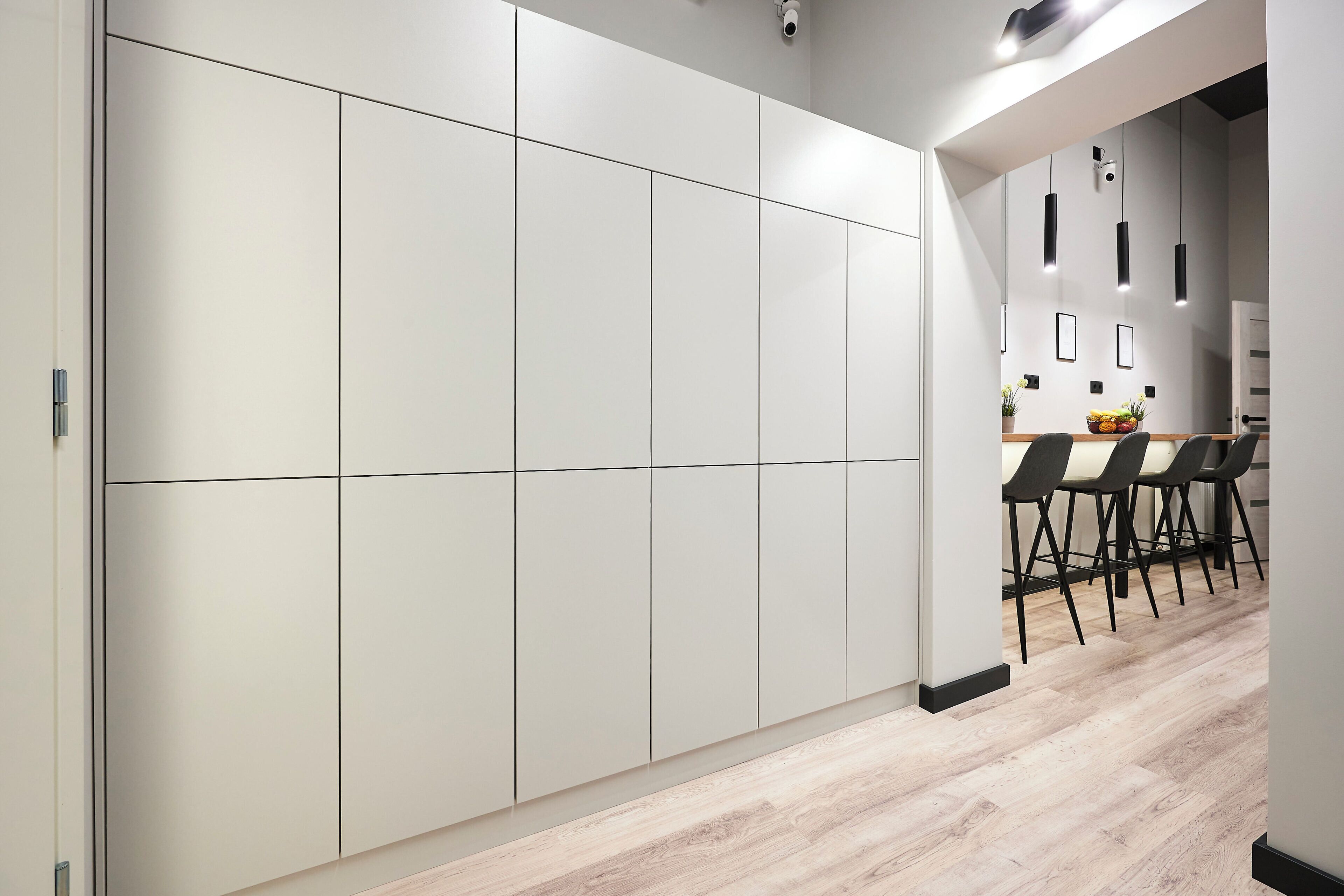 Una cocina moderna con un sistema de alacenas blancas empotradas, encimera de madera y comedor con sillas negras.