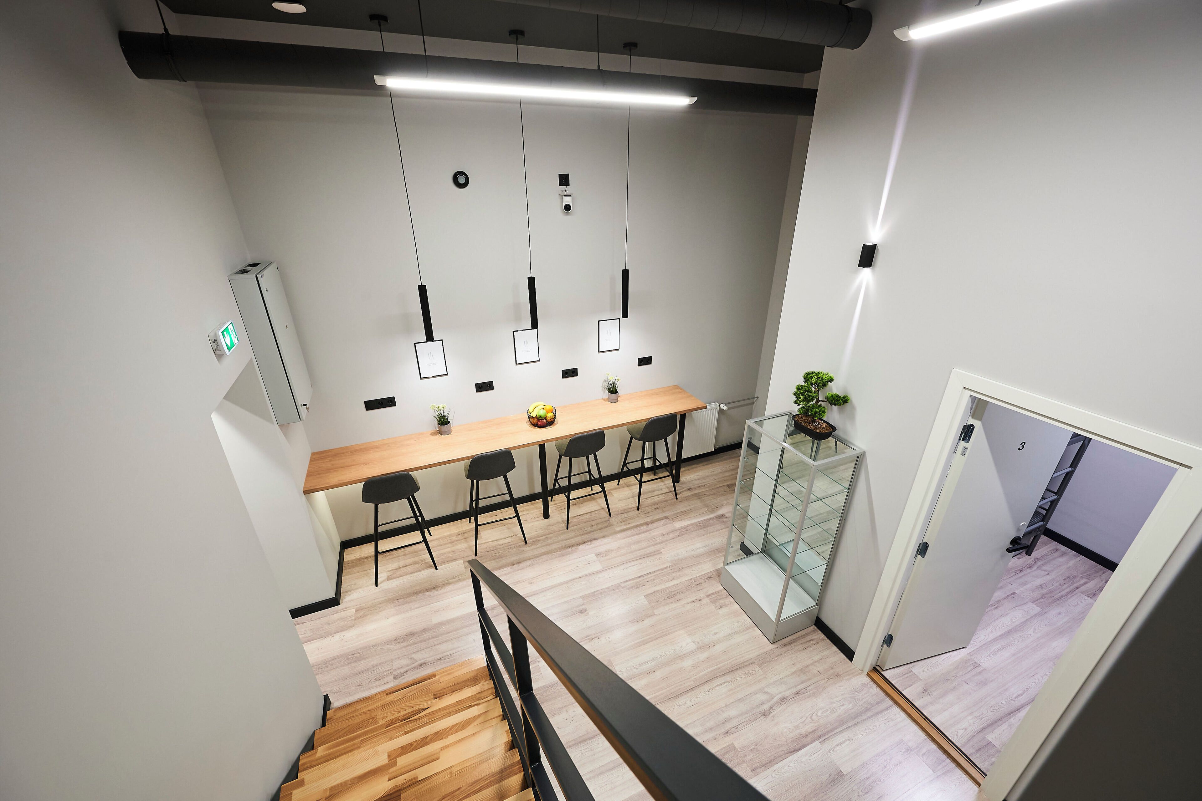 Un espacio de oficina moderno con una mesa de conferencias de madera, sillas negras, lámparas colgantes y una escalera que lleva a otro piso.