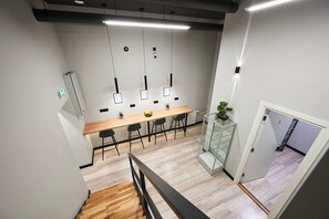 A modern office space with a wooden conference table, black chairs, pendant lights, and a staircase leading to another floor. - Nomad Boutique Hostel  (Tallinn)