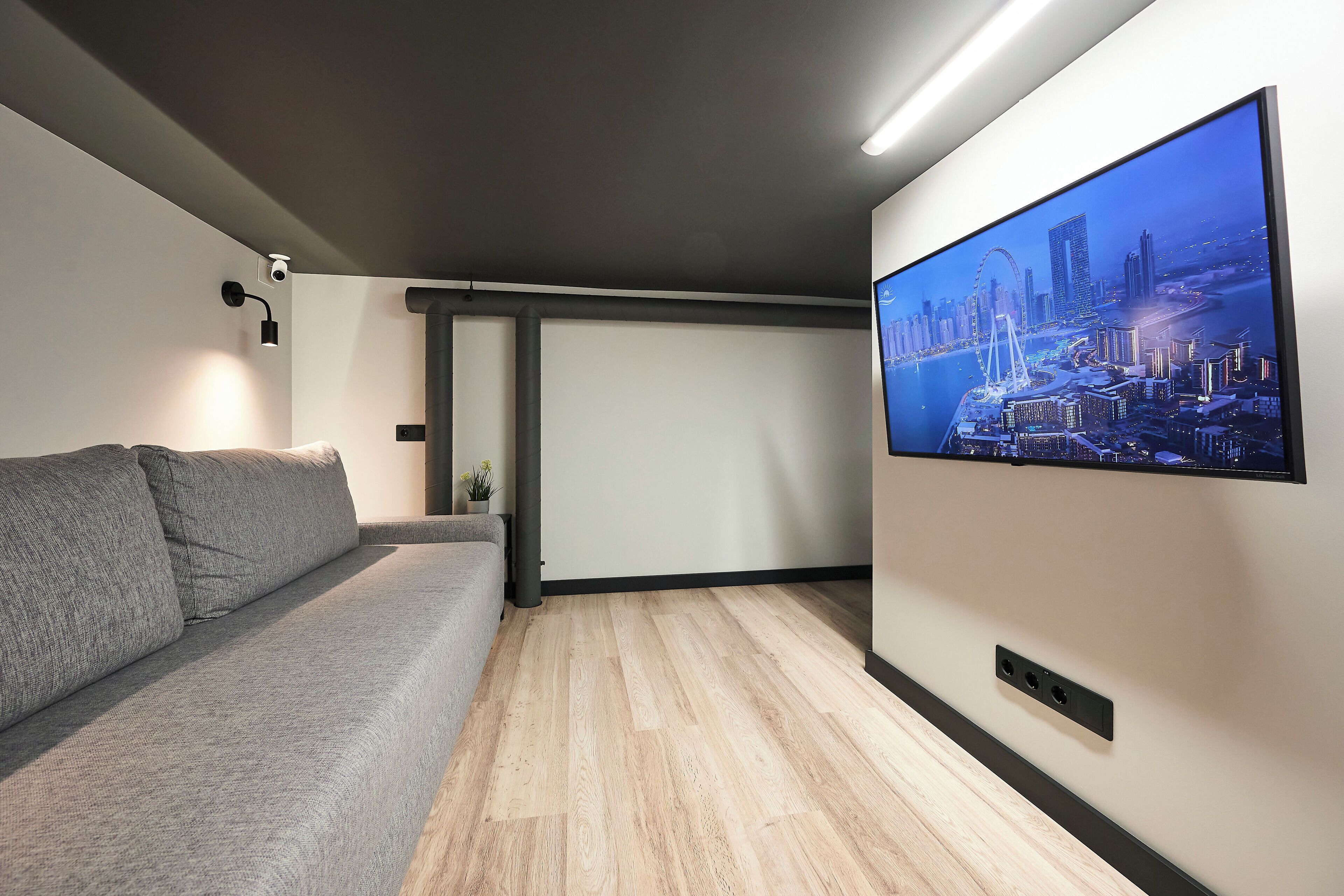 A modern living room with a large flat-screen TV mounted on the wall, a grey sofa, and a wooden floor.