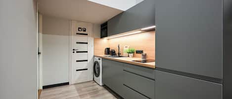 A modern kitchen with a washing machine, grey cabinets, a wooden countertop, and a small plant.