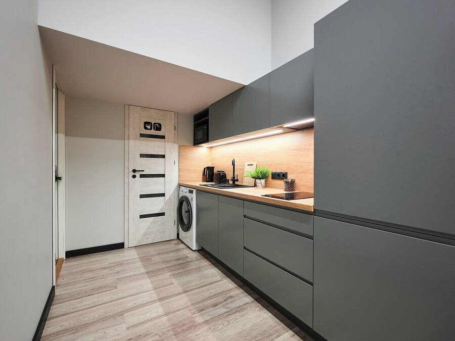 A modern kitchen with a washing machine, grey cabinets, a wooden countertop, and a small plant.