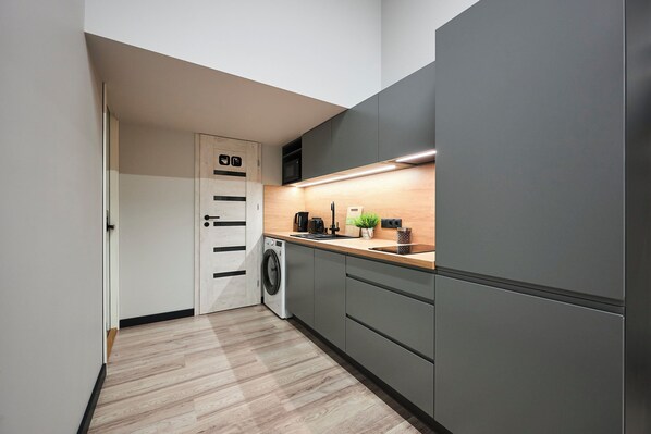A modern kitchen with a washing machine, grey cabinets, a wooden countertop, and a small plant. - Nomad Boutique Hostel  (Tallinn)