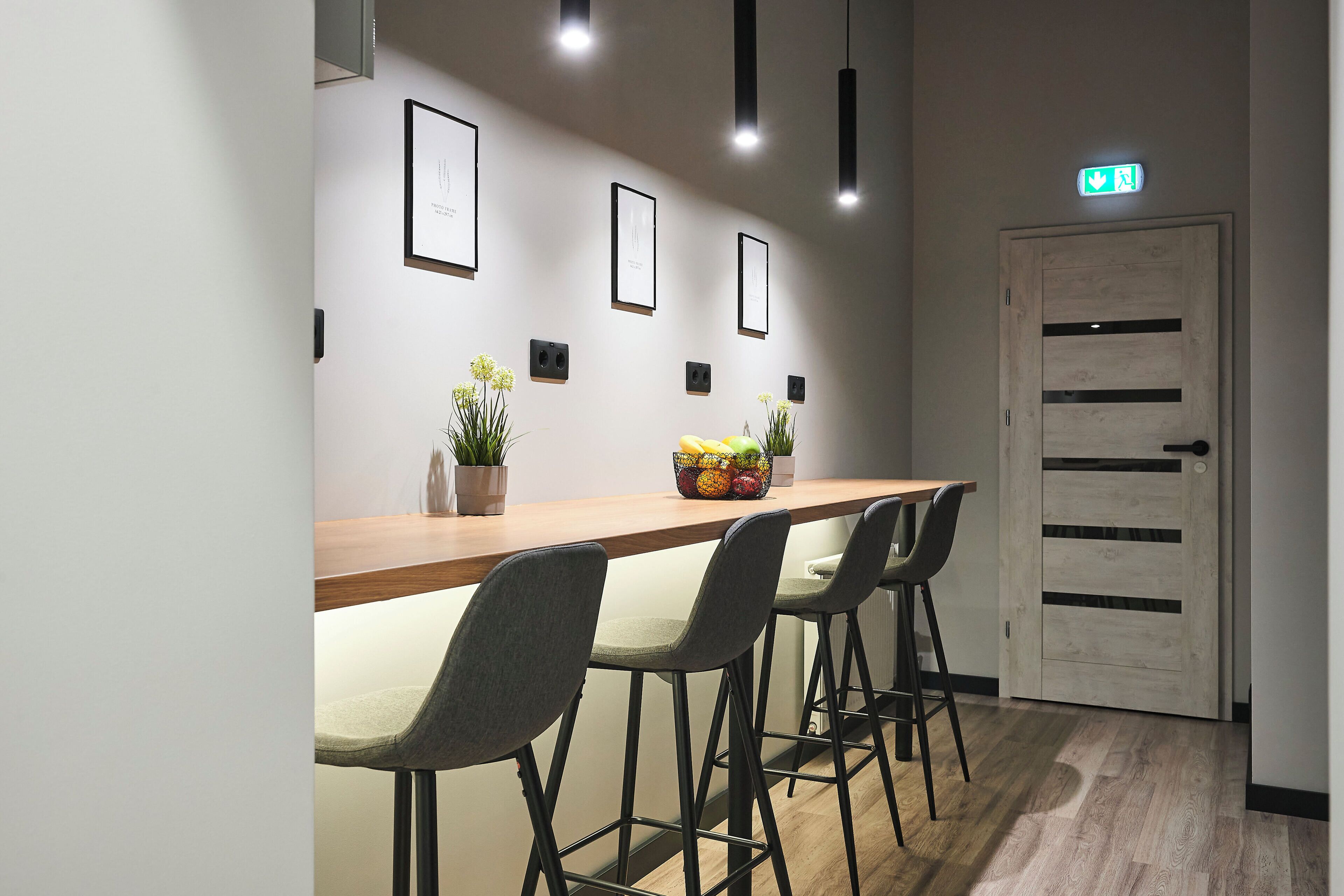 A modern interior with a long wooden table, four grey chairs, and framed pictures on the wall.