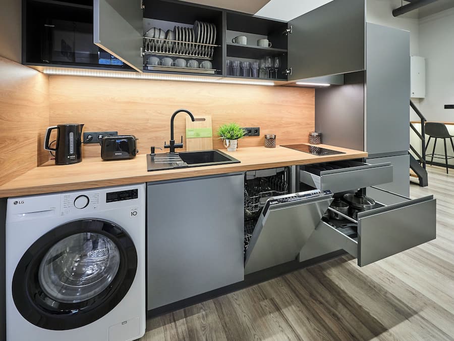 A compact kitchen with a built-in washing machine, a toaster, and a sink with a faucet.