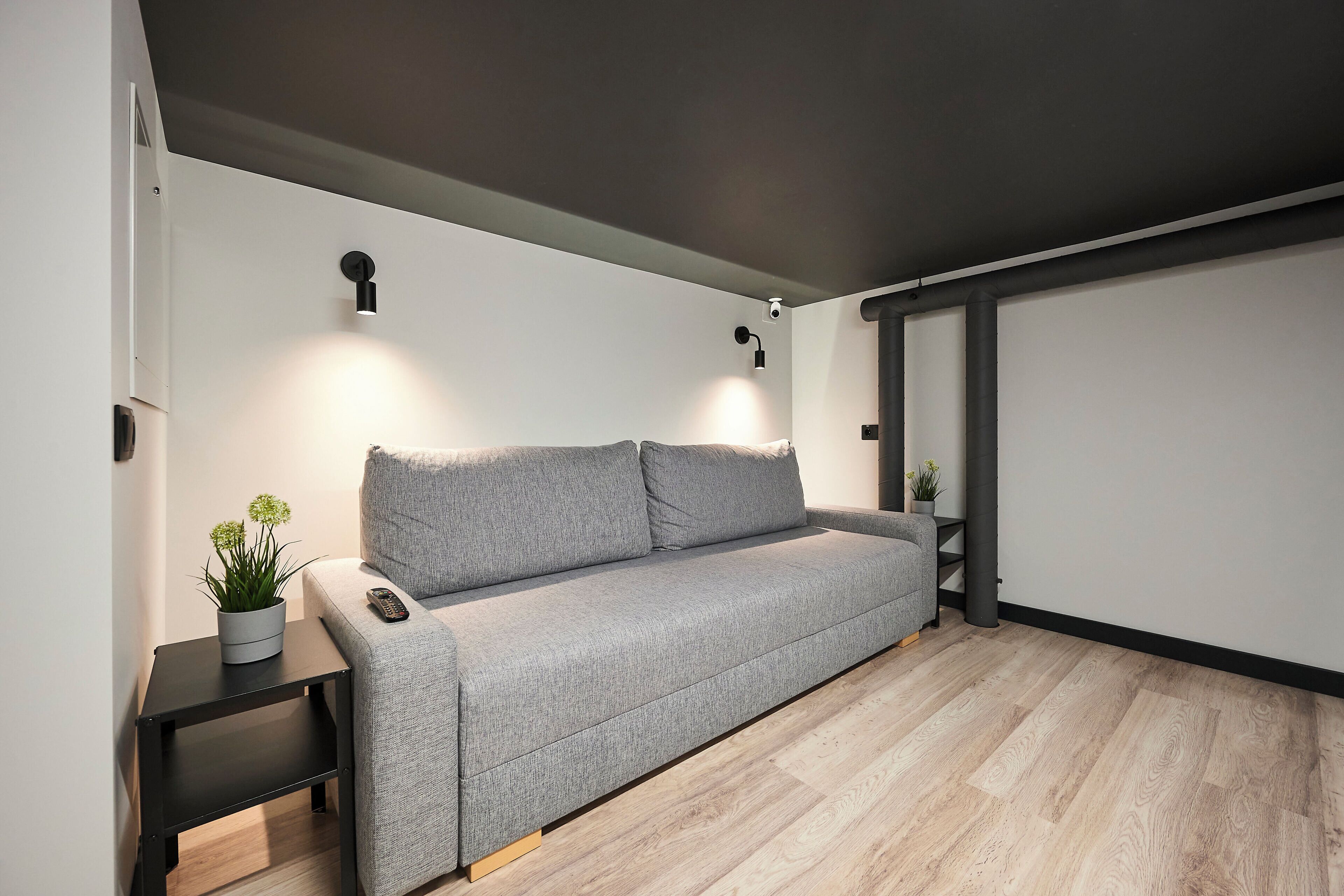 Una sala de estar moderna con un sofá gris, una mesita con una planta y una lámpara de pared.