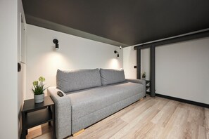 A modern living room with a grey sofa, a small table with a plant, and a wall-mounted light fixture. - Nomad Boutique Hostel  (Tallinn)