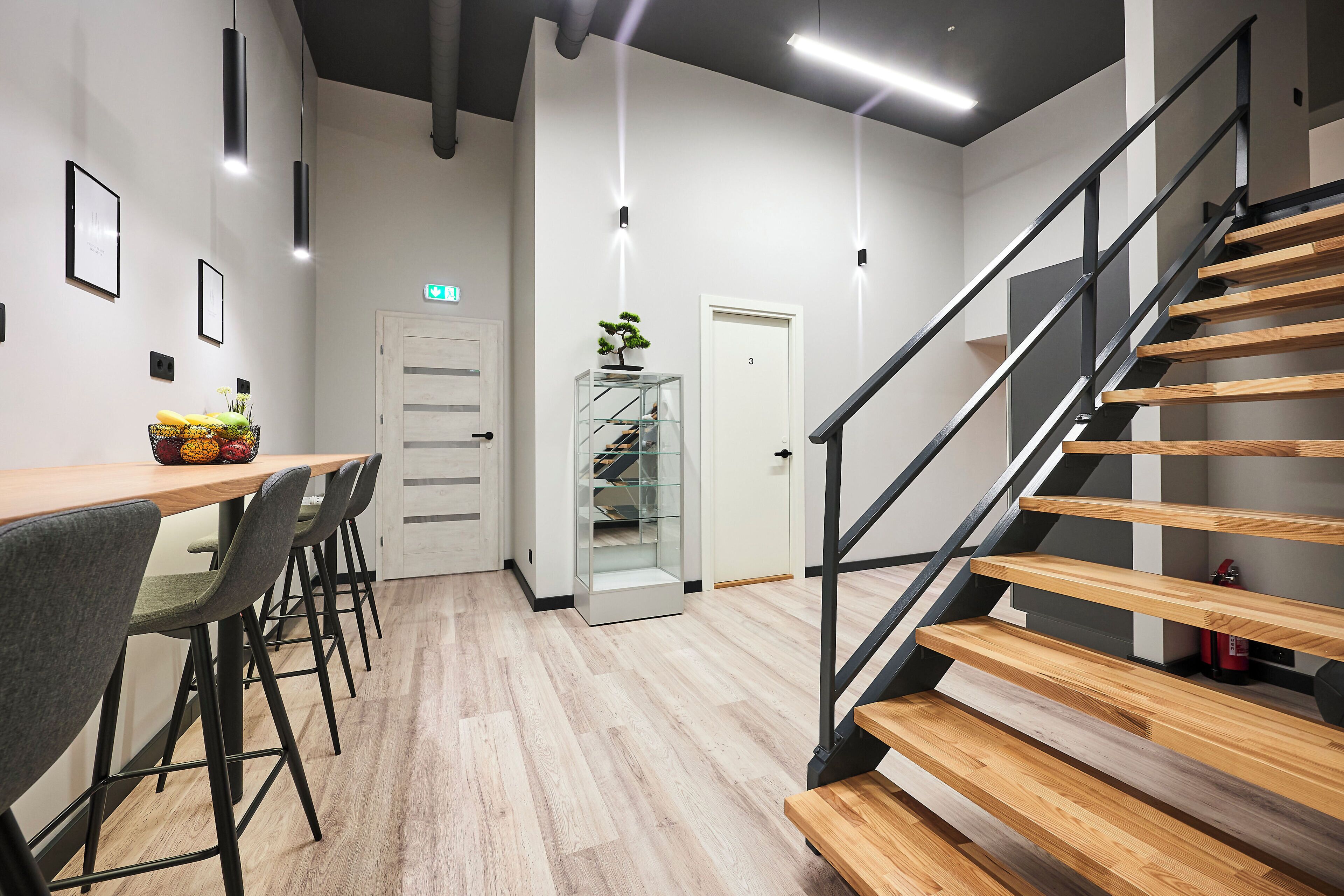 Un interior moderno con una escalera de madera, una zona de comedor con sillas, un expositor de vidrio y una puerta marcada con el número 3.