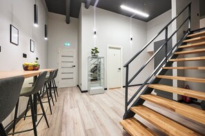 Un interior moderno con una escalera de madera, una zona de comedor con sillas, un expositor de vidrio y una puerta marcada con el número 3.