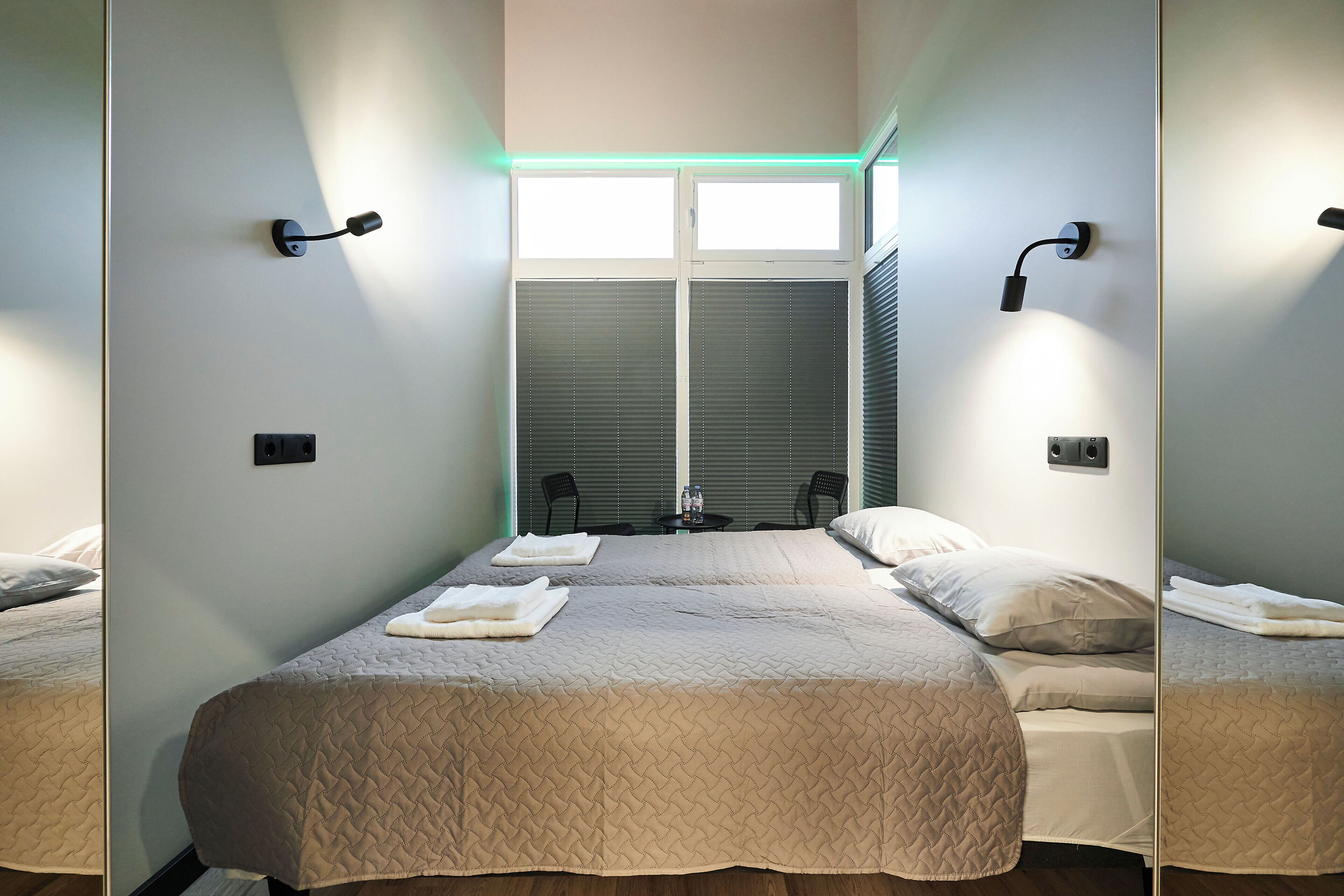 Habitación de hotel con dos camas, una ventana con persianas y una lámpara fijada a la pared.